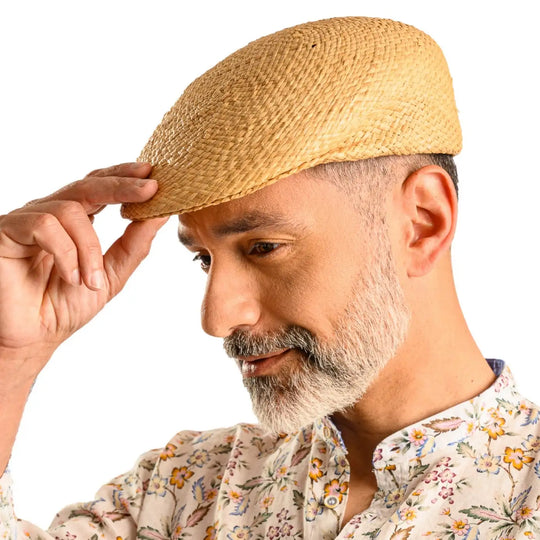 primo piano laterale inclinato di uomo con barba che indossa un coppola siciliana estiva in rafia color paglia realizzato da cappelleria primario nesti
