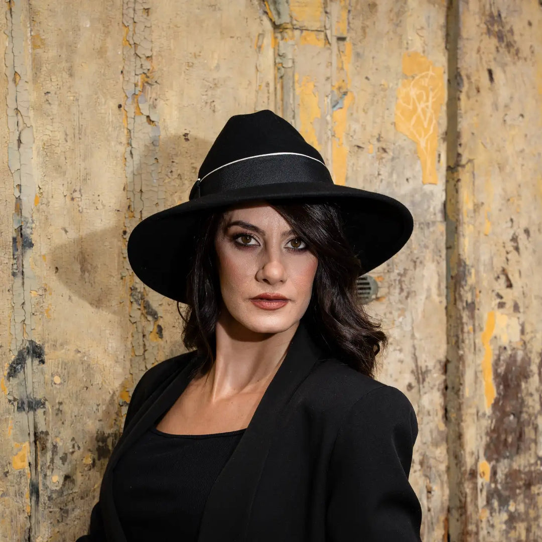 modella adulta con cappello signorile a tesa larga in feltro di lana merinos nero primario nesti total black su muro vintage