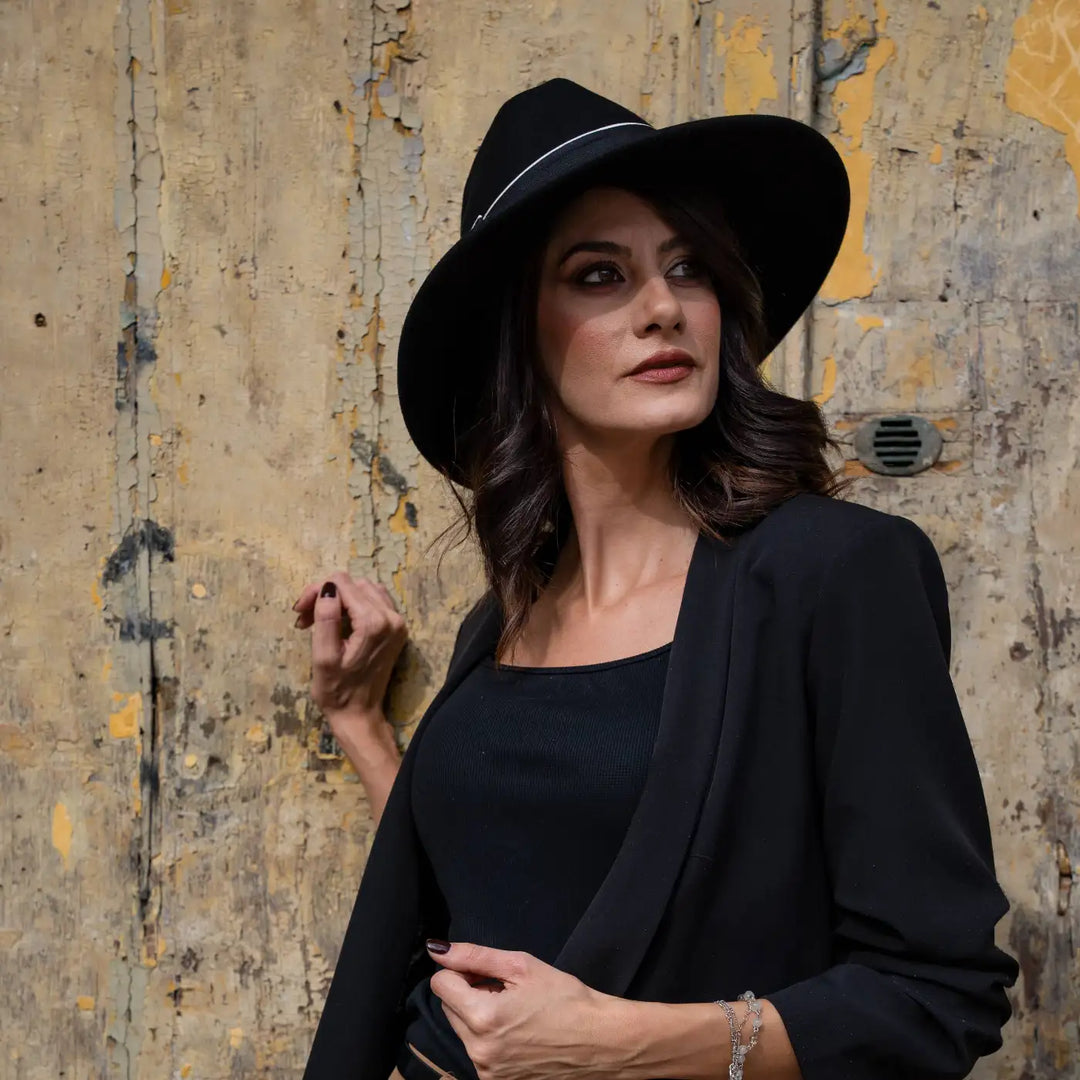modella adulta con cappello signorile a tesa larga in feltro nero primario nesti con blazer nero e pantalone beige in uno sfondo vintage