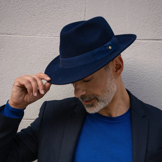 modello adulto con barba indossa un cappello fedora in feltro di morbido cashmere primario nesti blu di profilo con sfondo di muro bianco