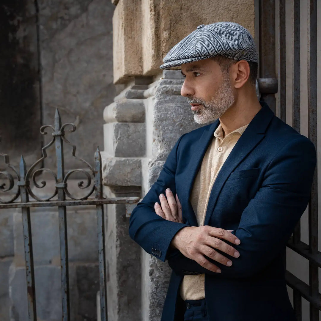 modello adulto con barba indossa una coppola peaky blinder spigata primario nesti con giacca blu navy in una posa sicura