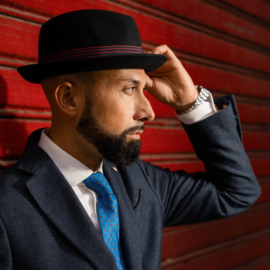 modello adulto ed elegante con cappello lobbia homburg in feltro raso di lapin primario nesti blu che guarda a destra completo blu scuro su sfondo rosso