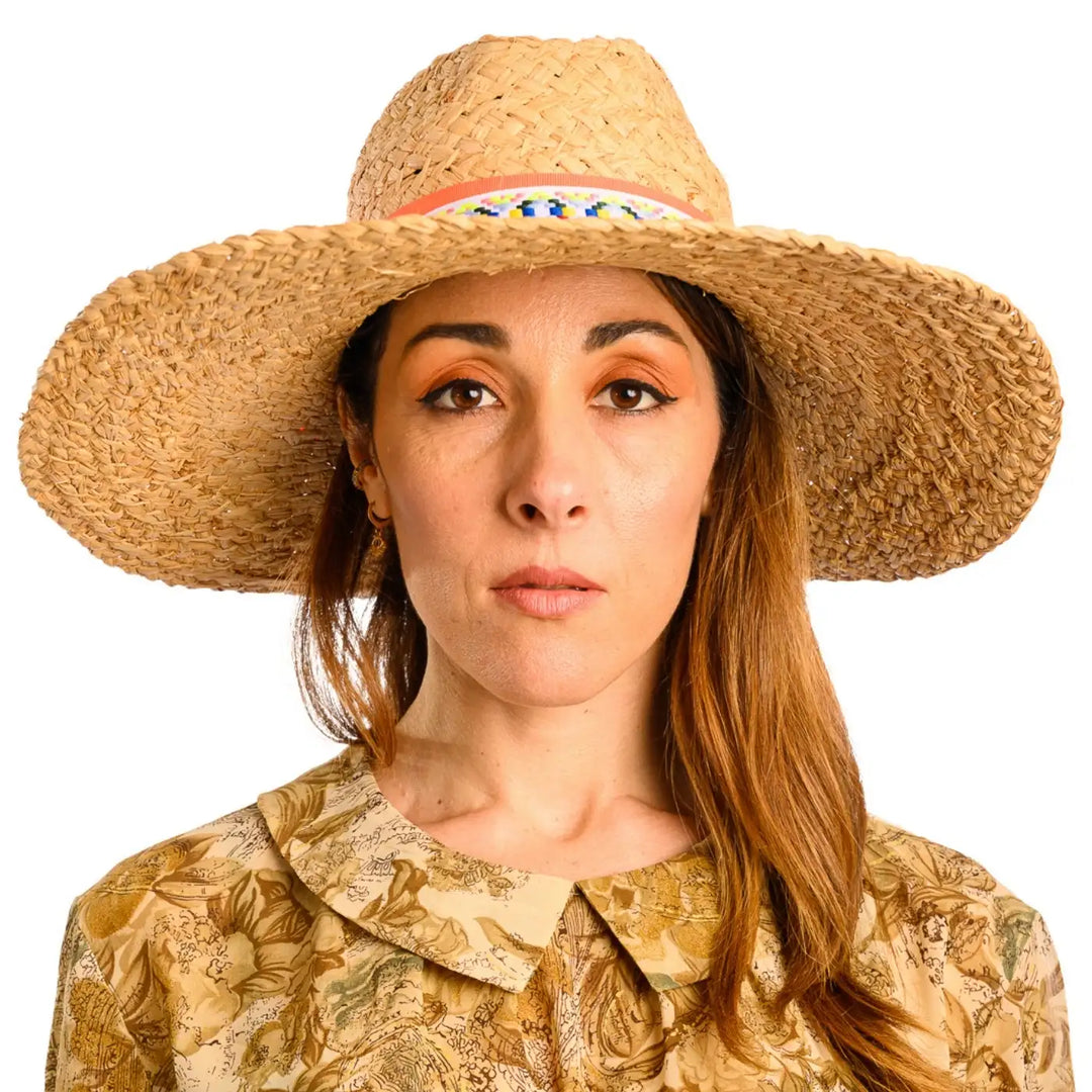 primo piano frontale di donna con capelli lunghi che indossa un cappello da mare a tesa larga in rafia color paglia arancio fatto da cappelleria primario nesti