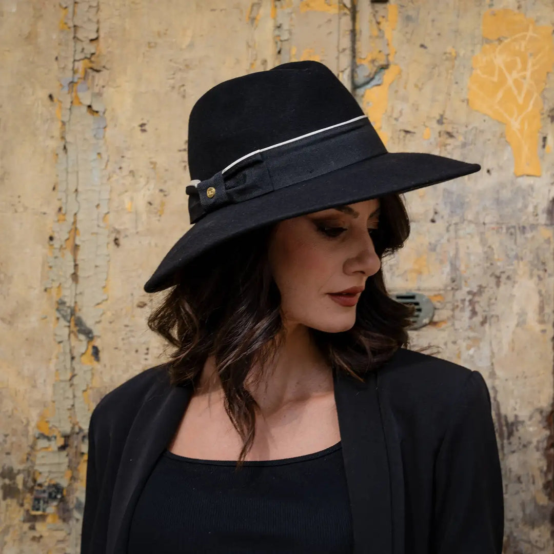 profilo di modella adulta con cappello signorile a tesa larga in feltro nero primario nesti e look total black su sfondo vintage