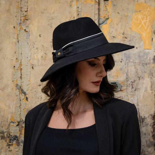 profilo di modella adulta con cappello signorile a tesa larga in feltro nero primario nesti e look total black su sfondo vintage